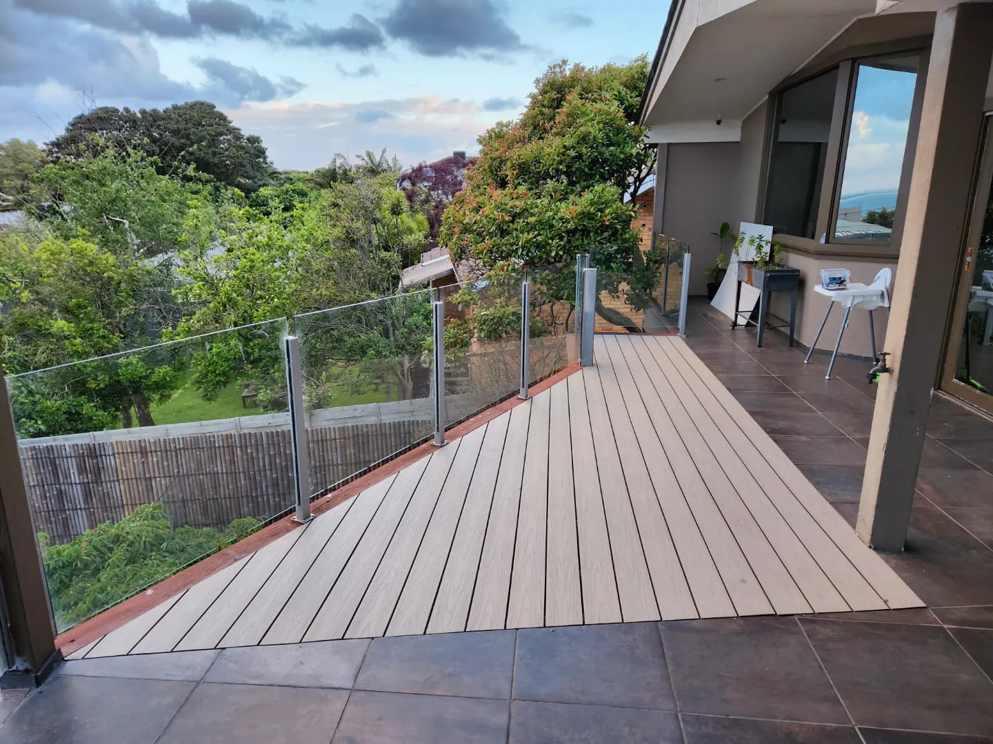 Composite timber deck with glass balustrade overlooking a leafy backyard